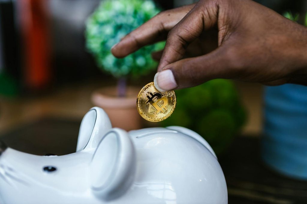 A close-up of a hand placing a bitcoin into a white piggy bank, symbolizing investment and savings.